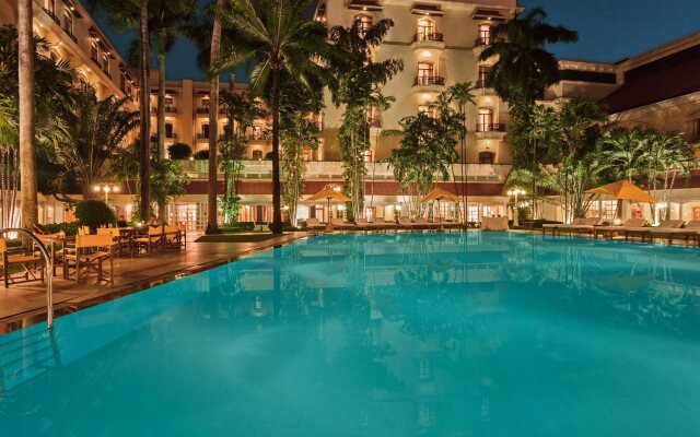 colonial façade of the oberoi grand in kolkata, featuring neoclassical arches, tall columns, and green-shuttered windows.