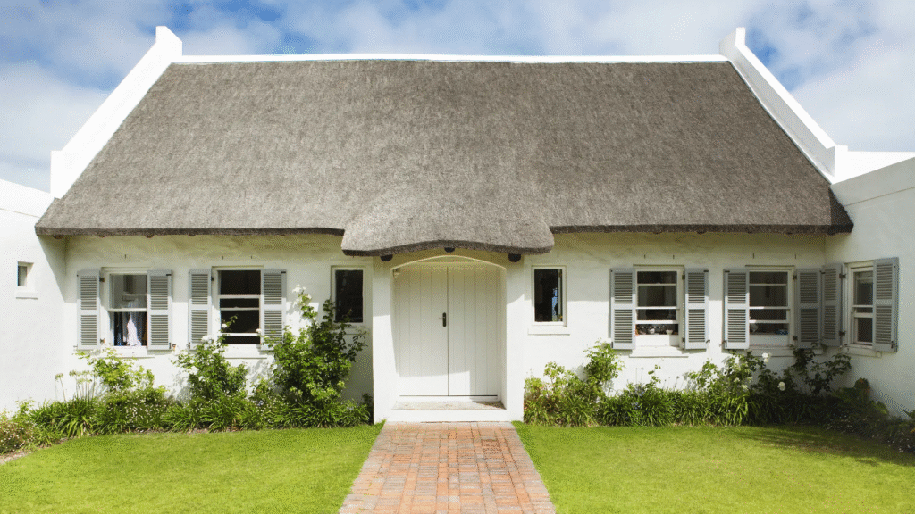 charming white bungalow with thatched roof, central wooden door, and manicured front lawn, perfect for cosy and functional living.